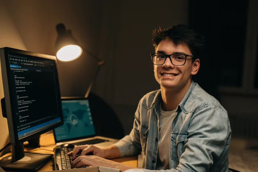 A smiling annotator wearing glasses works on data at his computer monitor late at night, representing the hands-on data annotation training provided by DeeLab Academy.
